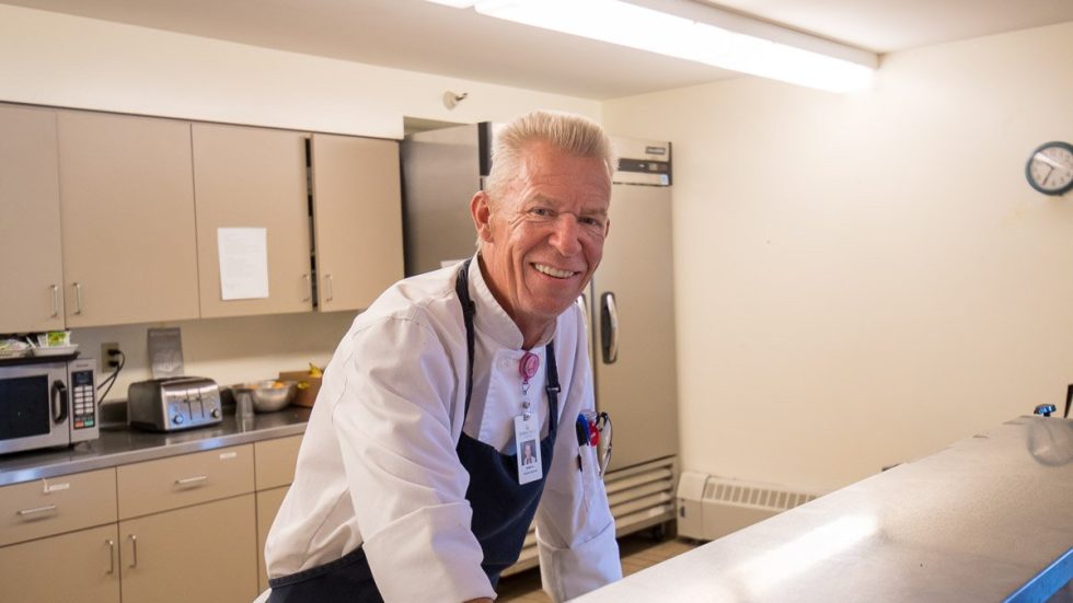 Friendly chef in a bright kitchen ready to serve nutritious meals for the community.