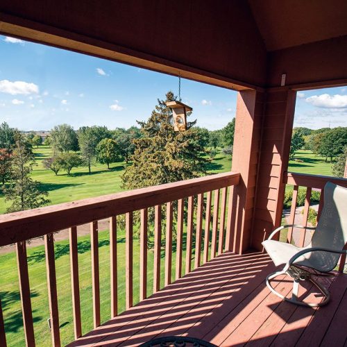 Balcony with a chair overlooking peaceful green lawns and trees under a bright blue sky.