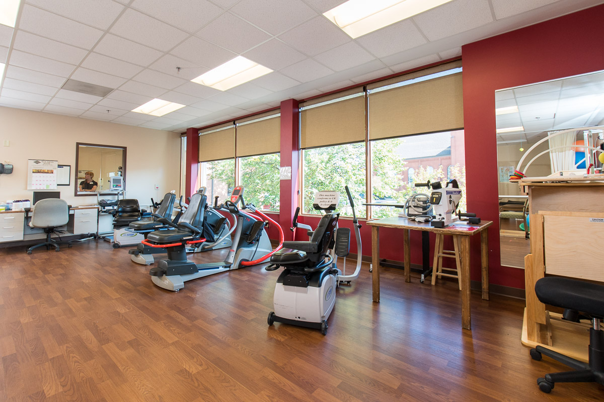 Bright fitness room with exercise equipment and large windows overlooking greenery, promoting wellness.
