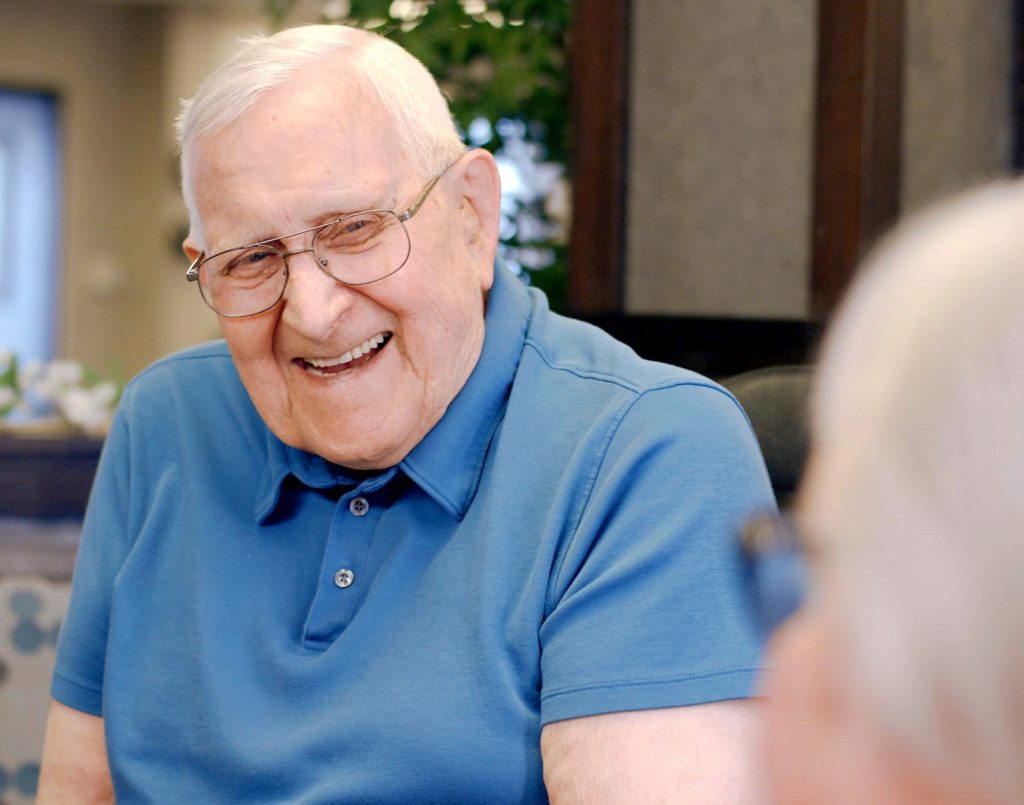 Elderly man in blue shirt sharing a joyful moment in a warm, welcoming community setting.