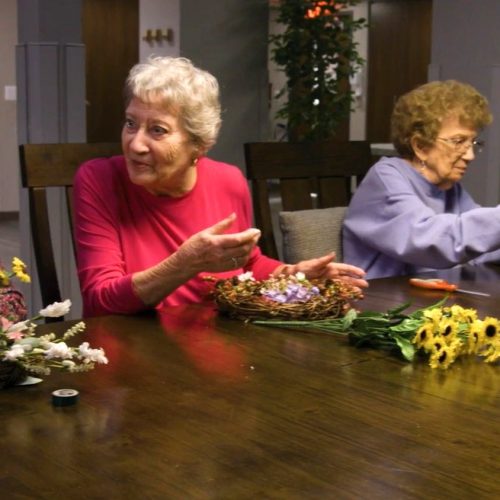 Seniors gather around a table, enjoying a relaxing flower arranging activity together.
