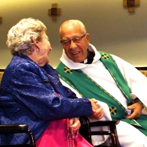 An elderly woman shares a warm, joyful moment with a caring chaplain in a peaceful gathering room.