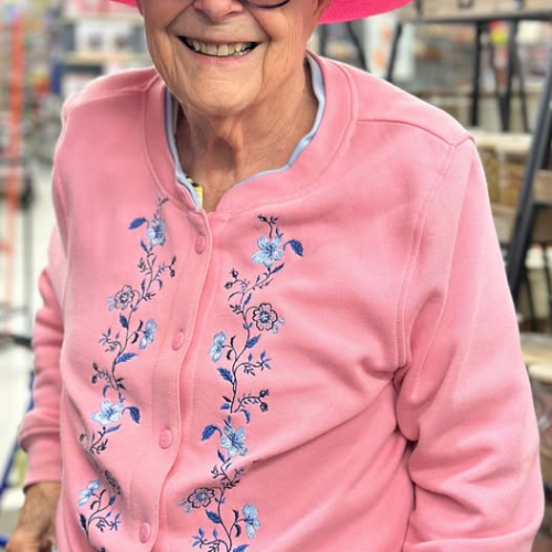 Senior woman smiling and wearing a pink hat while out shopping.