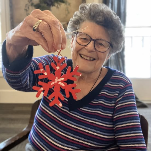 Senior woman smiling and holding painted snowflake craft.