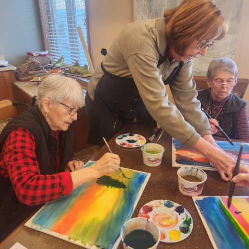 Three elderly women create landscape paintings.