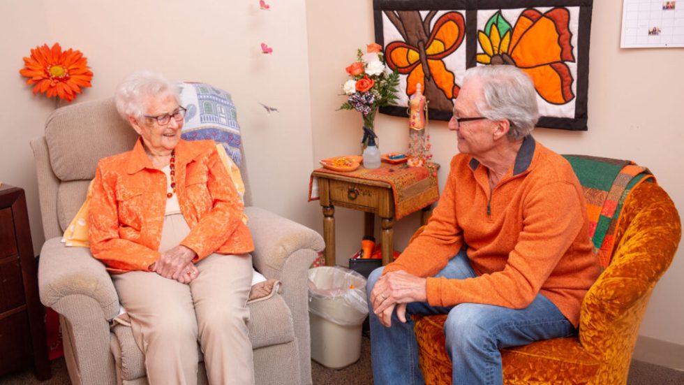 Two seniors enjoy a warm conversation in a bright, inviting room filled with colorful decor.