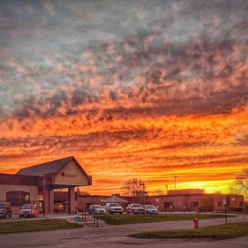 Sunset casting warm light over a welcoming community center with parked cars and trees.
