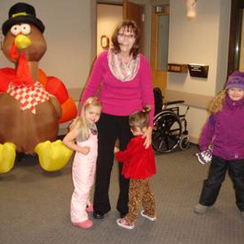 A warm gathering with children and a caregiver near a festive turkey decoration inside the community area.