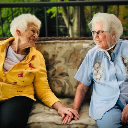 Two elderly women share a warm moment outdoors, enjoying friendship and peaceful surroundings.