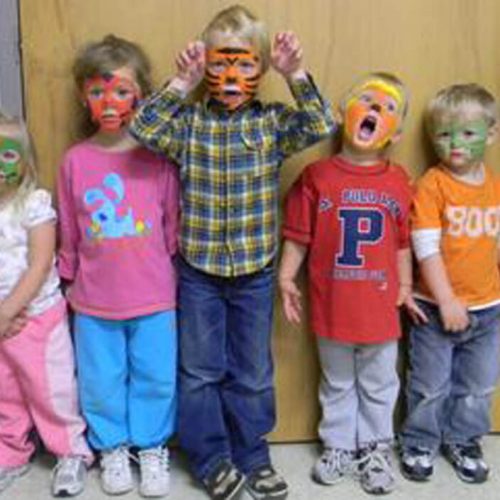Young children with colorful face paint enjoy a lively moment together indoors.