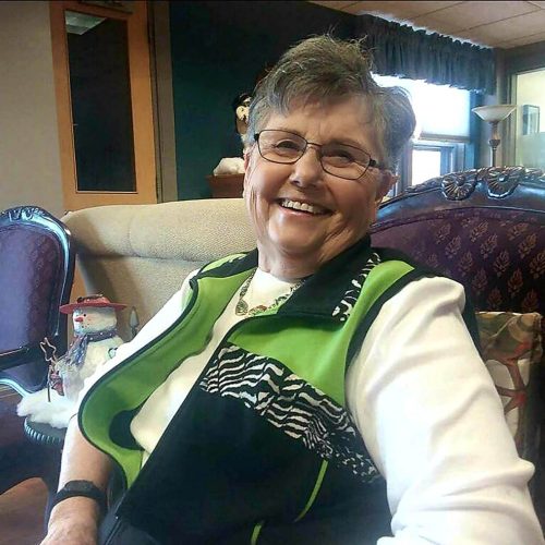 Smiling senior woman sitting comfortably in a warm, inviting living area with festive decor.