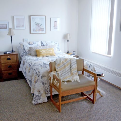 Sunlit bedroom with comfortable bed, wooden chair, and warm, inviting decor.
