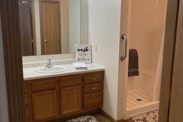 Bright, accessible bathroom with wood accents, safety grab bar, and welcoming decor for residents.