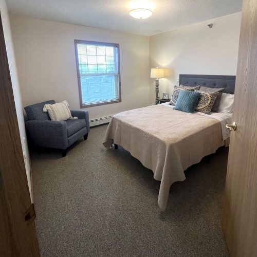 Bright bedroom with plush bedding, comfortable armchair, and warm lighting for restful living.