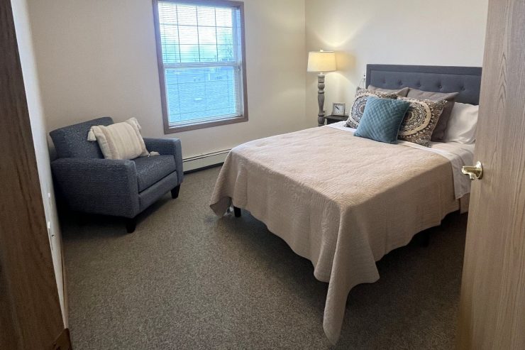 Bright bedroom with plush bedding, comfortable armchair, and warm lighting for restful living.