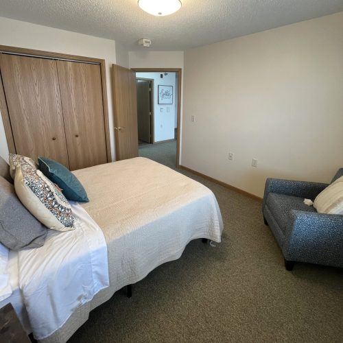 Sunlit bedroom with comfortable bed, inviting armchair, and a welcoming, peaceful atmosphere.