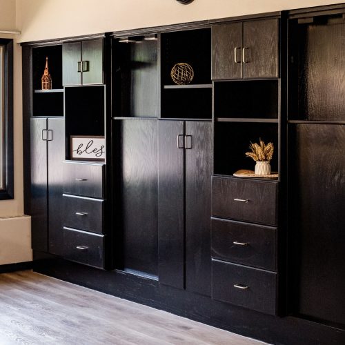 Dark wooden built-in storage with decor accents beneath a classic wall clock in a warm living space.