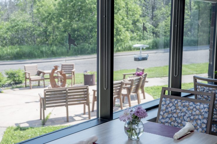 Bright dining area with floral decor overlooks a sunny outdoor patio with seating and greenery.