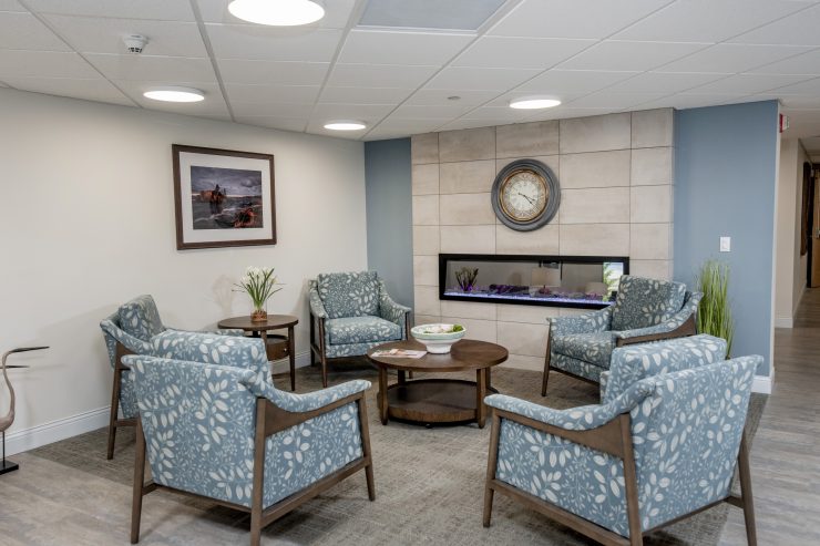 Comfortable seating area with patterned chairs around a table near a modern fireplace and wall clock
