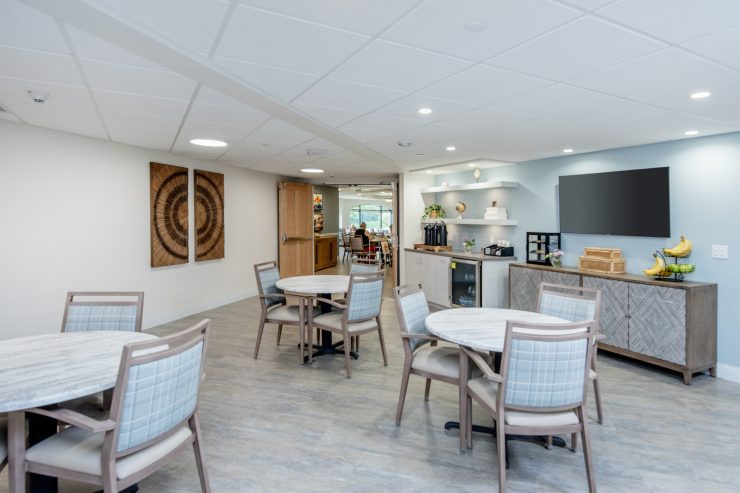 Bright common room with comfortable seating, dining tables, and a small refreshment area.