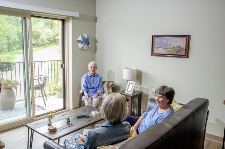Seniors enjoying a bright, welcoming living room with large windows and friendly conversation.