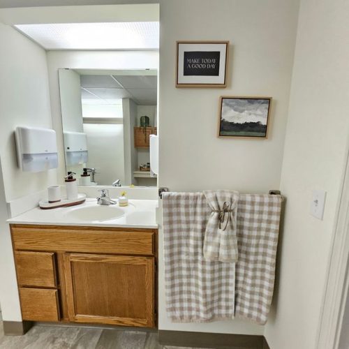 Bright bathroom vanity with wood cabinetry, soft lighting, and uplifting wall art promoting positive living.