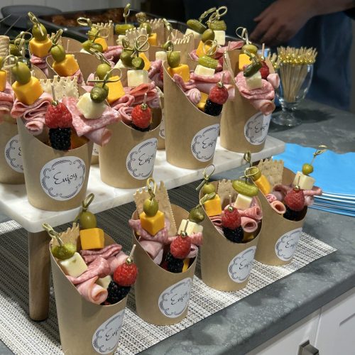 Individual snack cups with meats, cheeses, fruits, and crackers set for a community gathering.