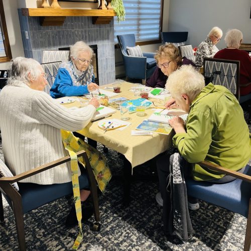 Seniors enjoying a group painting activity in a bright, inviting community room.