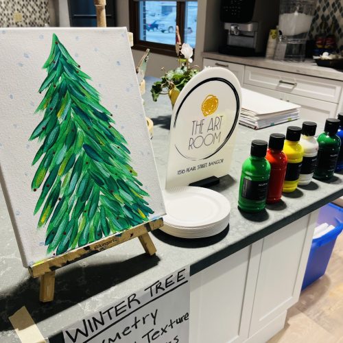 Art supplies and a winter tree painting set up in a bright, inviting community art room.