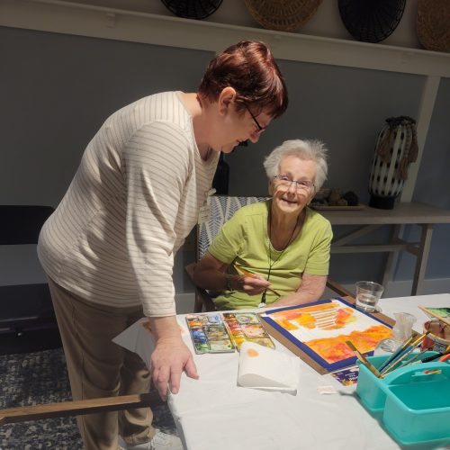 An associate helping a sneior resident with a painting activity.