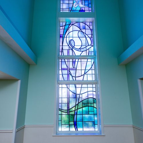 Tall stained glass window with abstract designs brightening a calm, welcoming space.