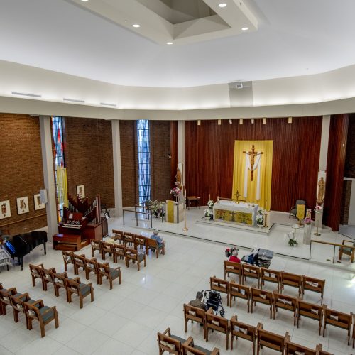 Spacious chapel with stained glass windows, wooden pews, and seniors gathered for quiet reflection.