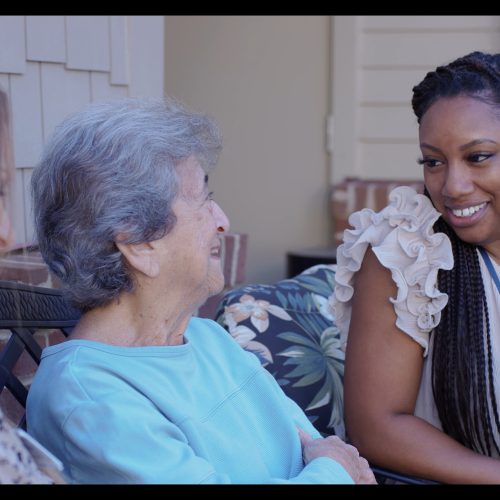 Three women sharing smiles and conversation on a comfortable outdoor patio setting.