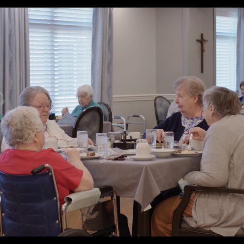 Seniors enjoying a meal and conversation in a bright, welcoming community dining room.