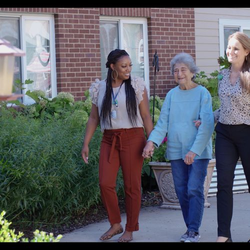 Three women enjoying a peaceful garden walk outside a welcoming retirement community.