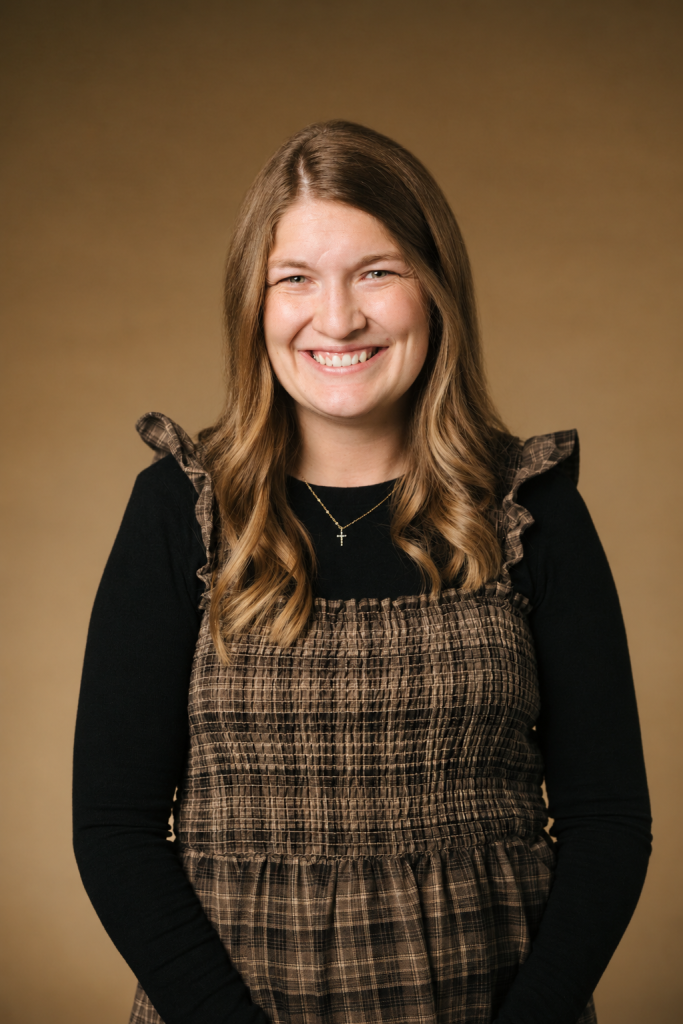 Smiling woman with warm expression in casual attire against a soft brown background.