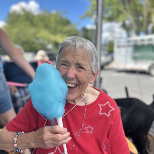 Senior woman enjoying a sunny day outdoors with friends, holding bright blue cotton candy.