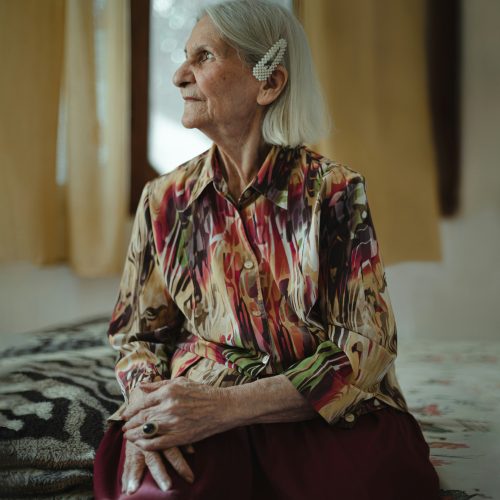 Elderly woman with a gentle smile enjoys a peaceful moment by the window in a warm room.