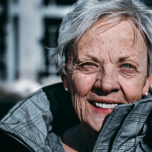 Smiling elderly woman in warm jacket enjoying an outdoor moment, radiating warmth and community.