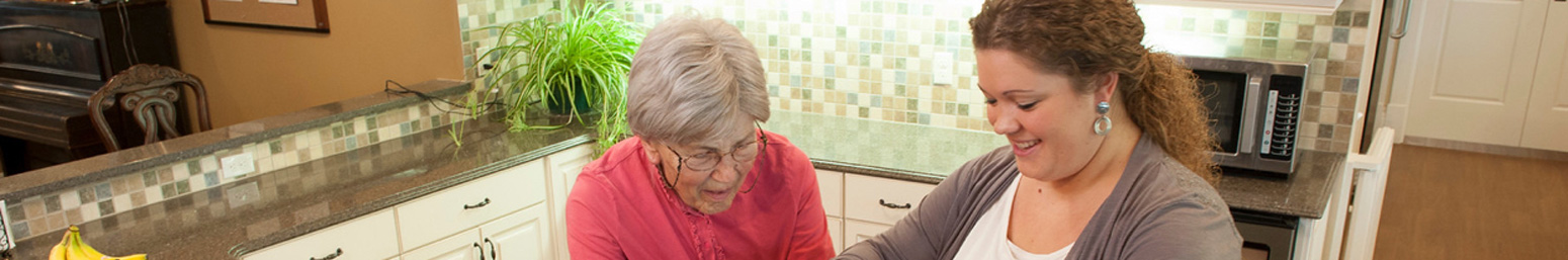 A senior living staff member helps an elderly woman in her kitchen