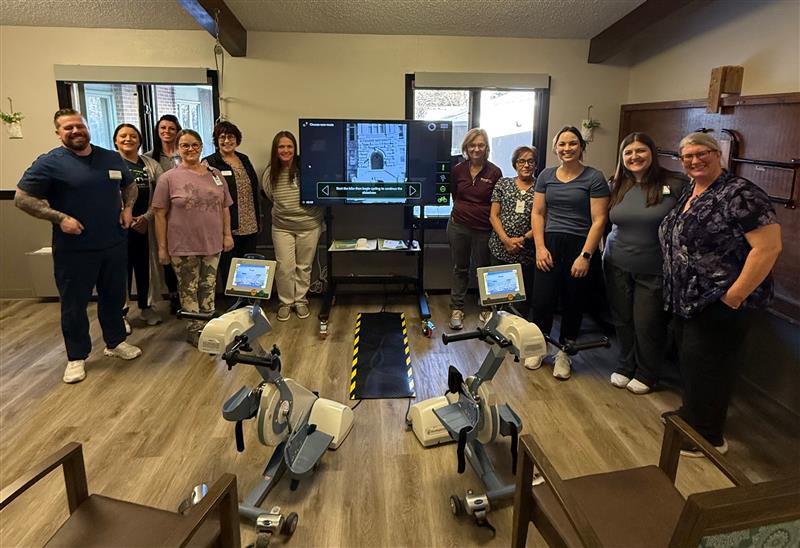 A group of staff smiling together in a bright, welcoming therapy room with exercise bikes.