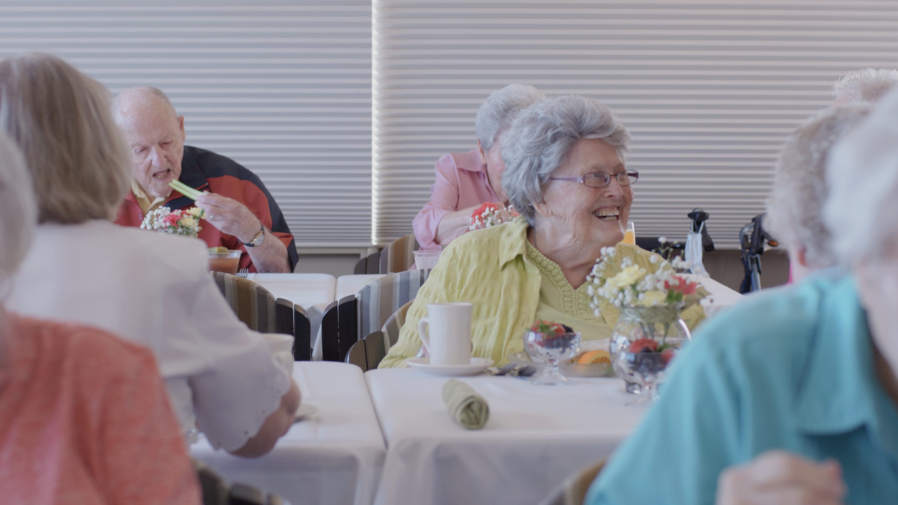 Seniors sharing a joyful meal together in a bright, welcoming dining room with floral décor.